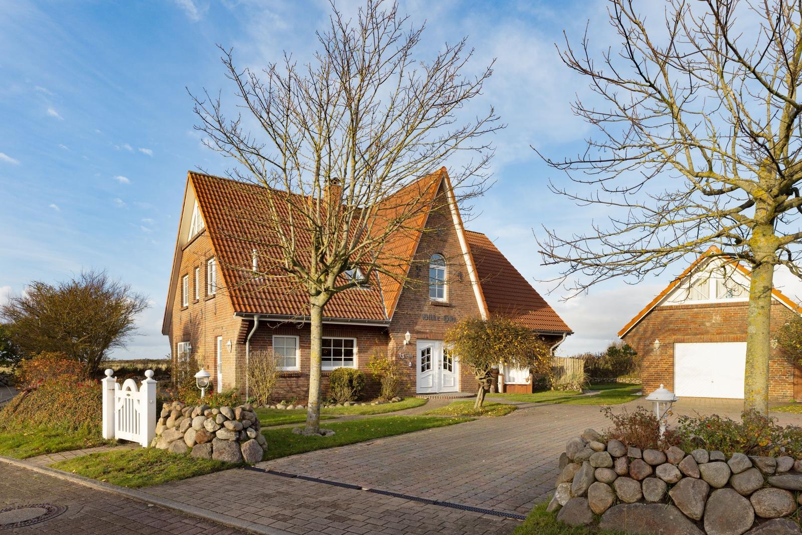 Ein zweistöckiges Haus mit rotem Ziegeldach und weißer Tür. Vor dem Haus führt ein gepflasterter Weg.