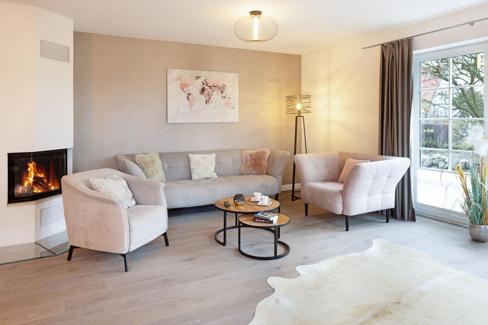 Wohnzimmer mit Sofa, zwei Sesseln, Kamin und Glasfront. Holzboden und Weltkarte an der Wand.