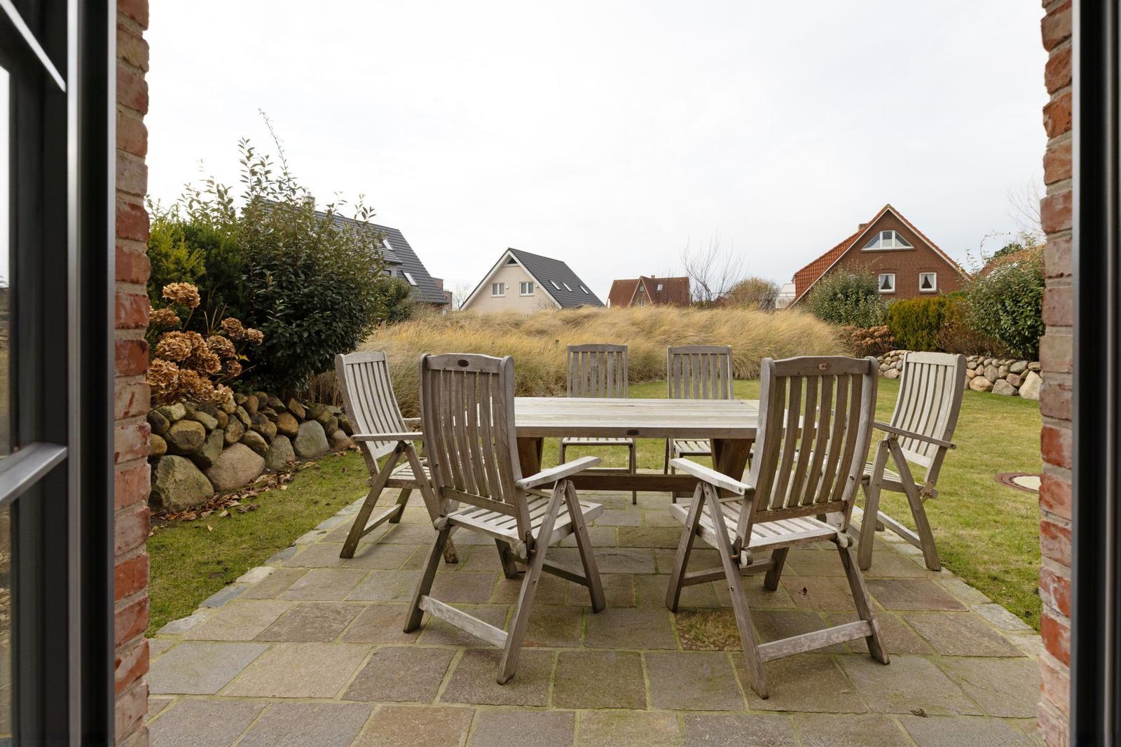 Terrasse mit Holztisch und Stühlen, Blick auf Garten und Nachbarhäuser.