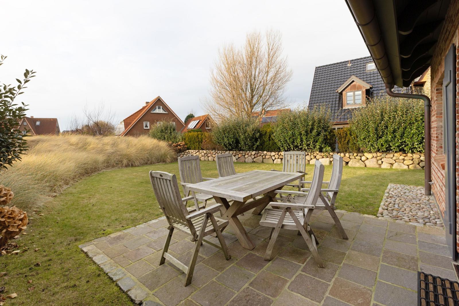 Terrasse mit Holztisch und Stühlen, umgeben von Grünfläche und Steinmauer.