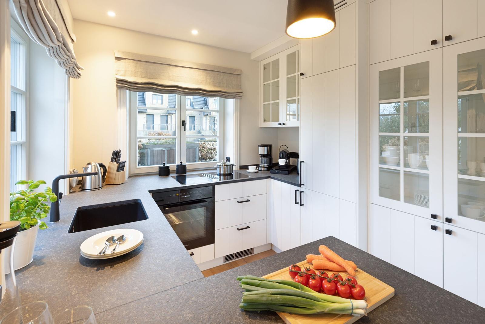 Moderne Küche mit weißen Schränken, dunklem Arbeitsplatz und Fensterblick.