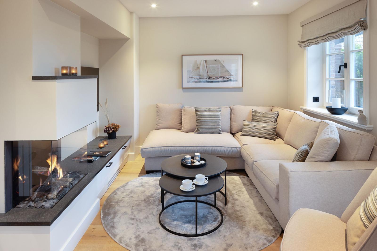 Ein Wohnzimmer mit Ecksofa, Kamin und runden Tischen auf Teppich.