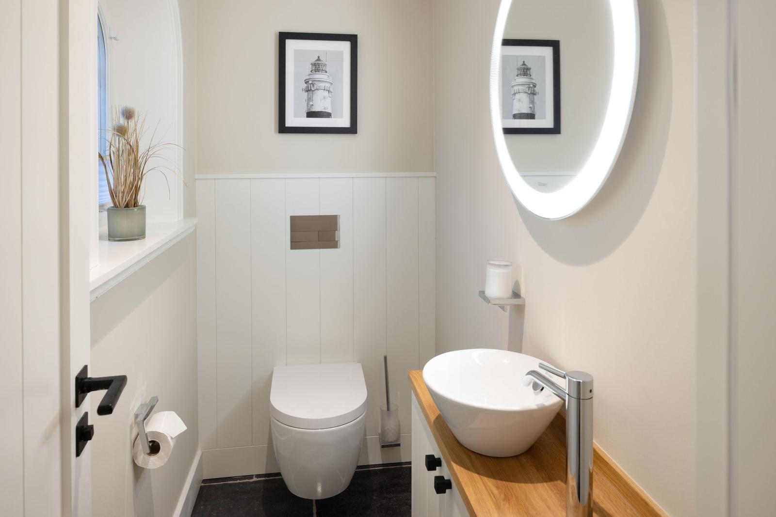 Badezimmer mit Toilette, Waschbecken und runden Spiegel. Wandbild zeigt Leuchtturm.