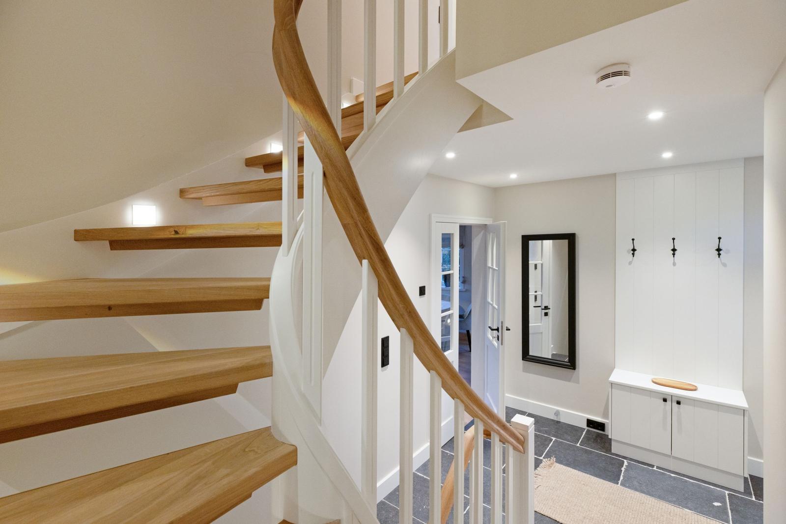 Eine Treppe mit Holzstufen und weißem Geländer führt in den Flur. An der Wand hängen drei Haken.