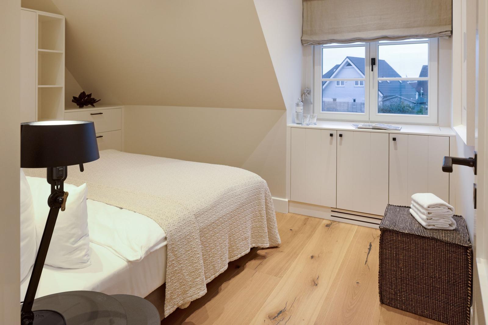 Schlafzimmer mit Bett, Schrank und Fenster. Holzboden und weiße Möbel.