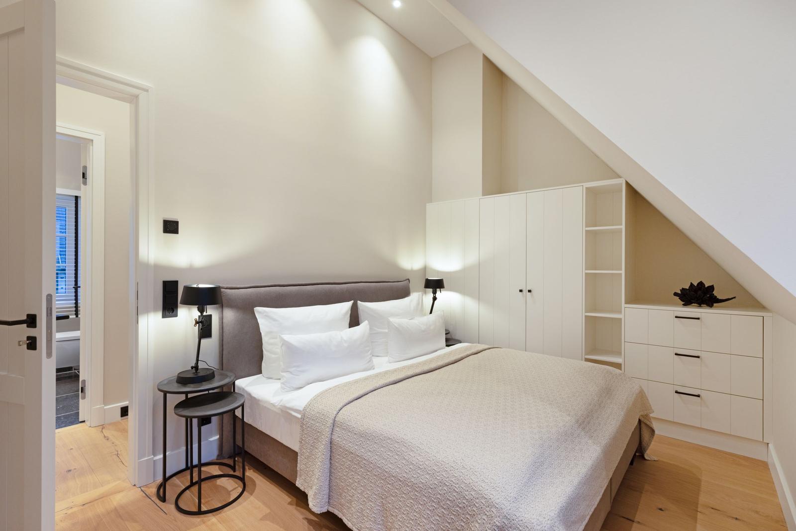 Schlafzimmer mit Bett, Nachttisch und Kleiderschrank unter Dachschrägen.