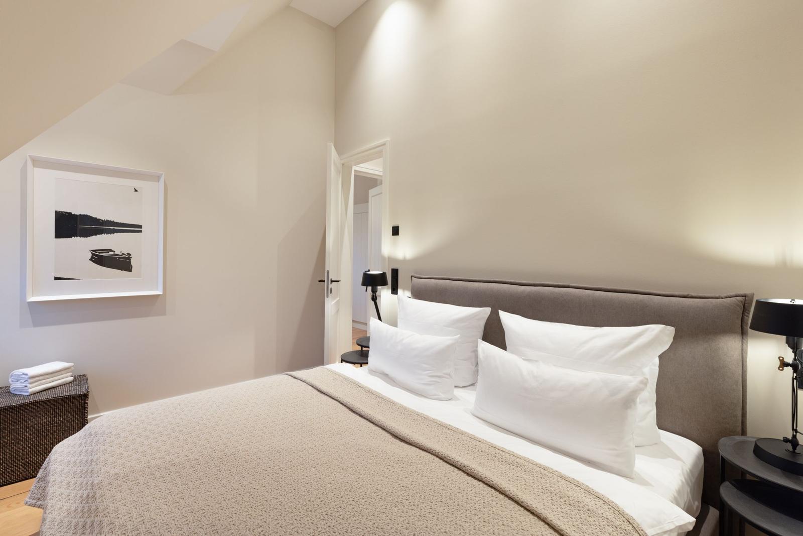 Schlafzimmer mit Bett, Kissen und Wandbild. Tür führt in einen Flur.
