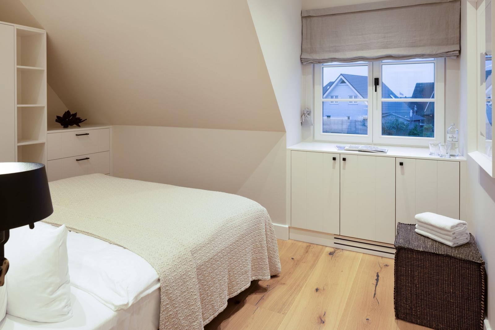 Schlafzimmer mit Dachschräge, Bett, Schrank und Fenster mit Blick.