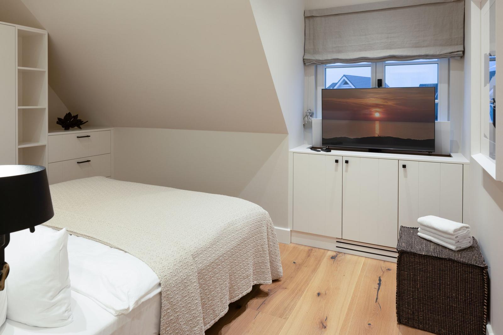 Schlafzimmer mit Dachschrägen, Bett, Fernseher und Holzboden.