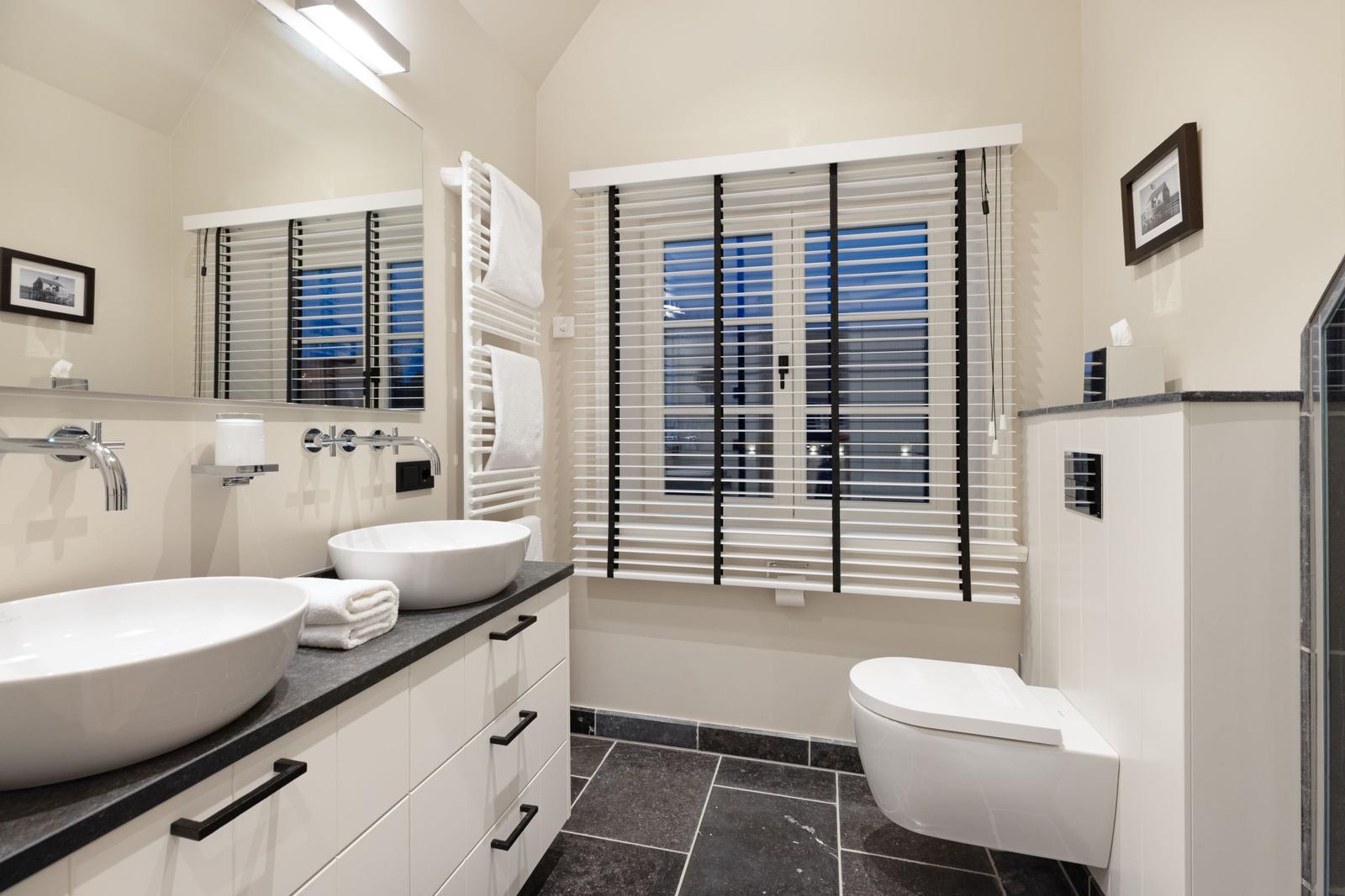 Badezimmer mit zwei Waschbecken, Toilette und Fenster mit Jalousie.