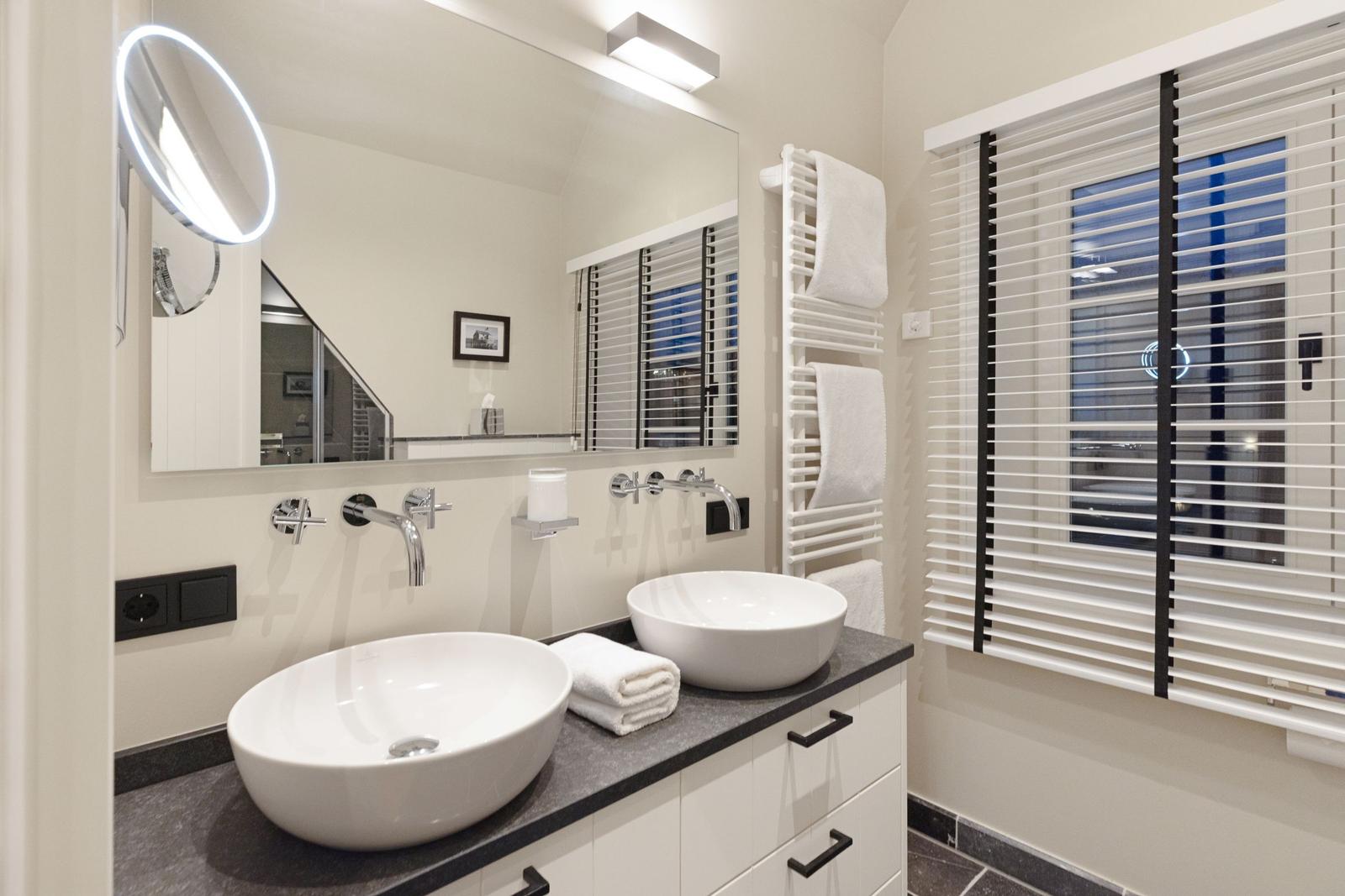 Badezimmer mit zwei Waschbecken, Spiegel und Fenster mit Jalousie.
