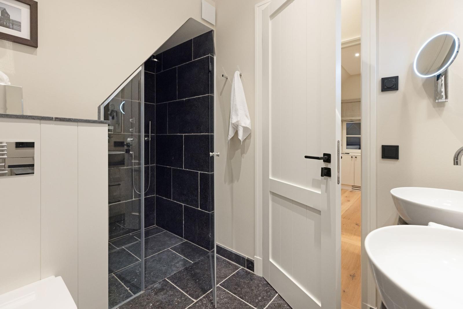 Badezimmer mit Dusche, Waschbecken und Tür zu angrenzender Wohnung.