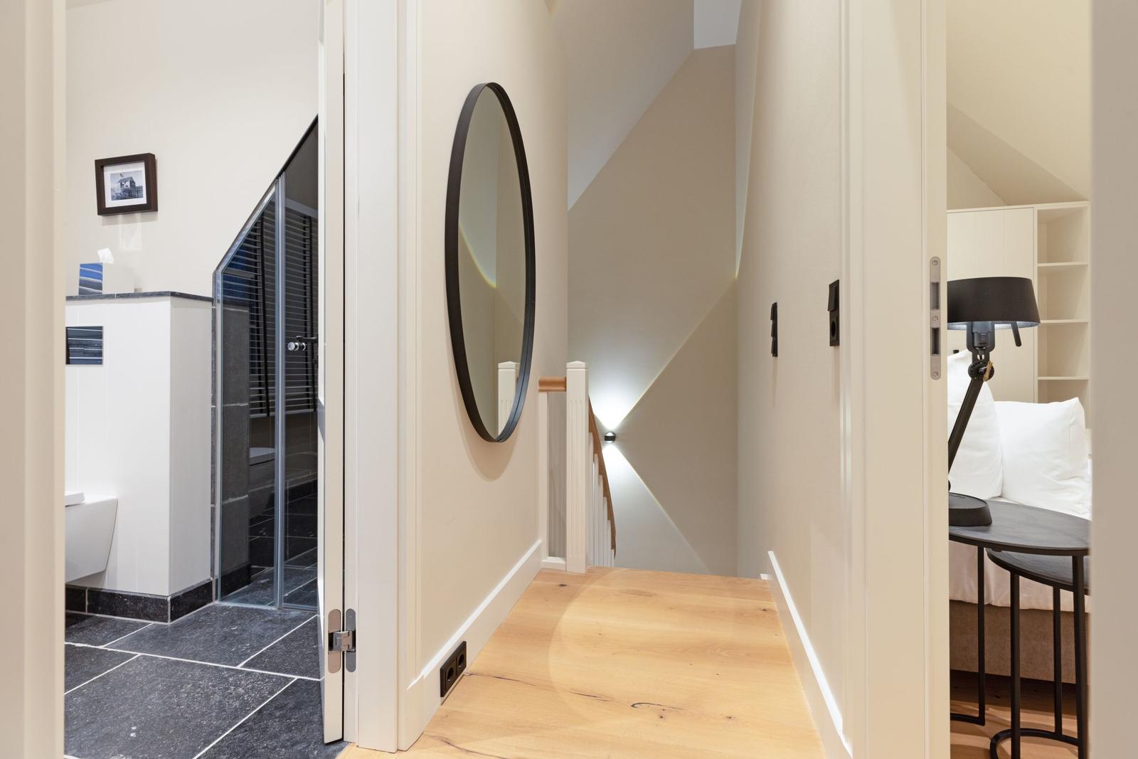 Flur mit Holzboden, runden Spiegel und Blick in Bad und Schlafzimmer.
