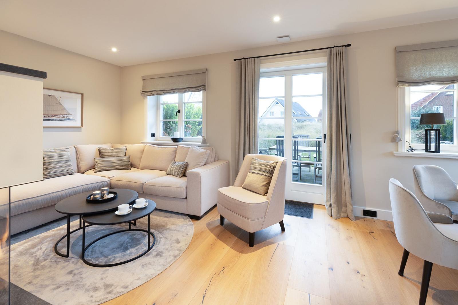 Wohnzimmer mit Sofa, Sessel und Tisch. Durchgangstür zum Balkon. Holzboden und Fenster.