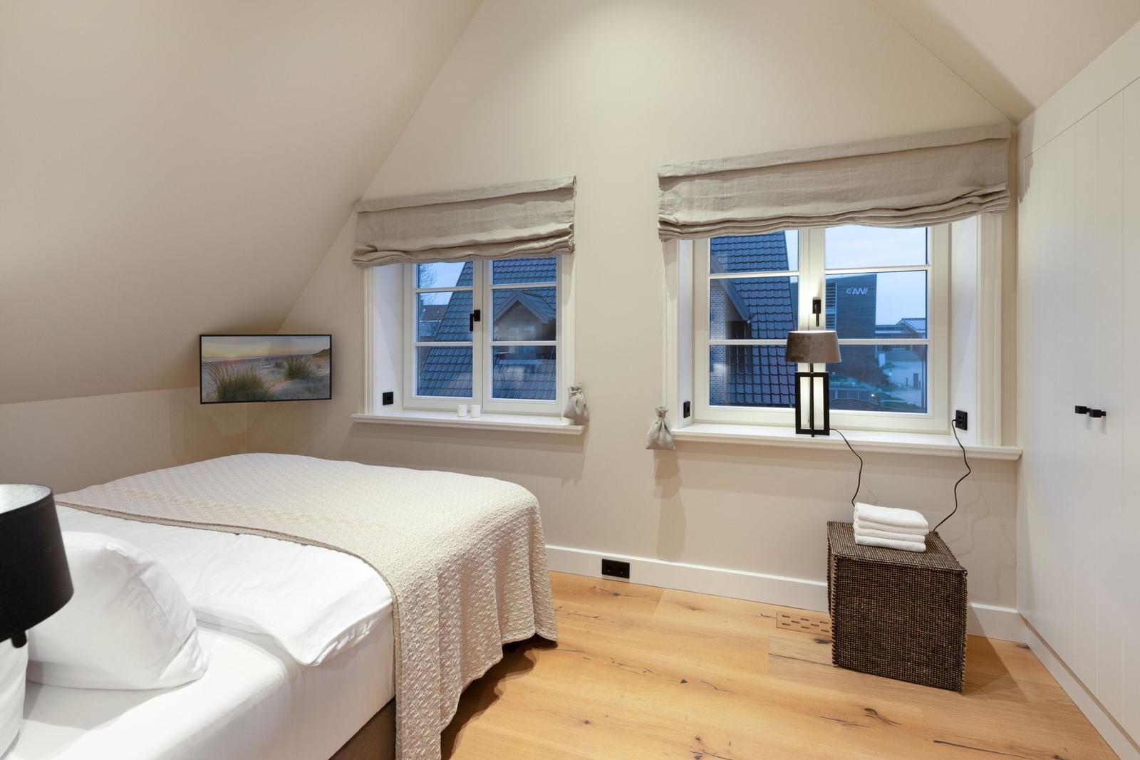 Schlafzimmer mit Dachfenster, zwei Fenstern und Holzboden.