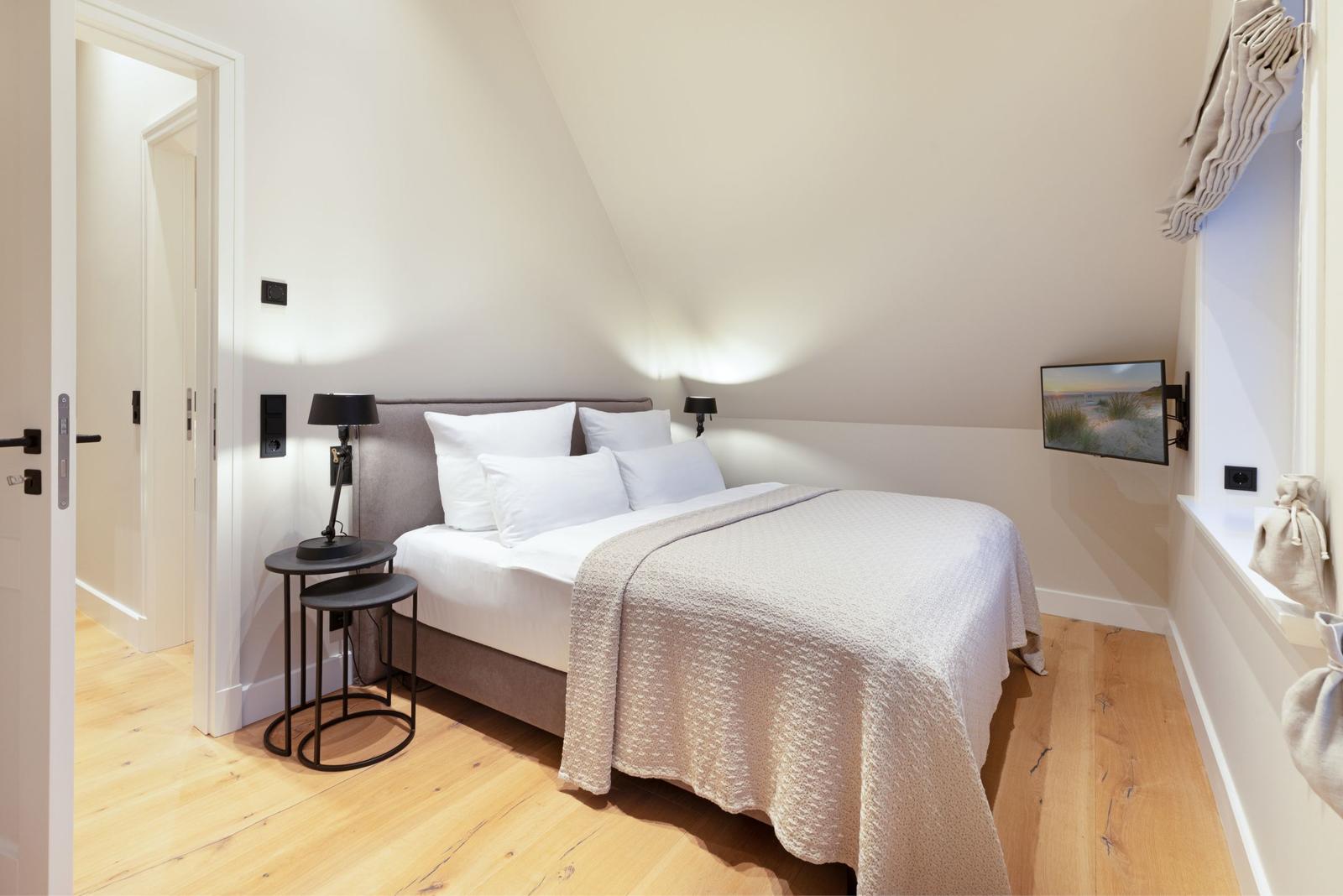Schlafzimmer mit Dachschrägen, Bett, Nachttisch und Wand-TV.