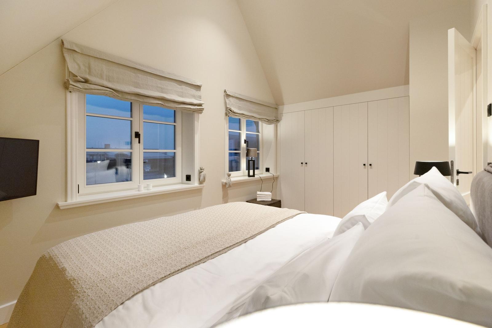 Schlafzimmer mit Dachschrägen, zwei Fenstern und einem großen Bett.
