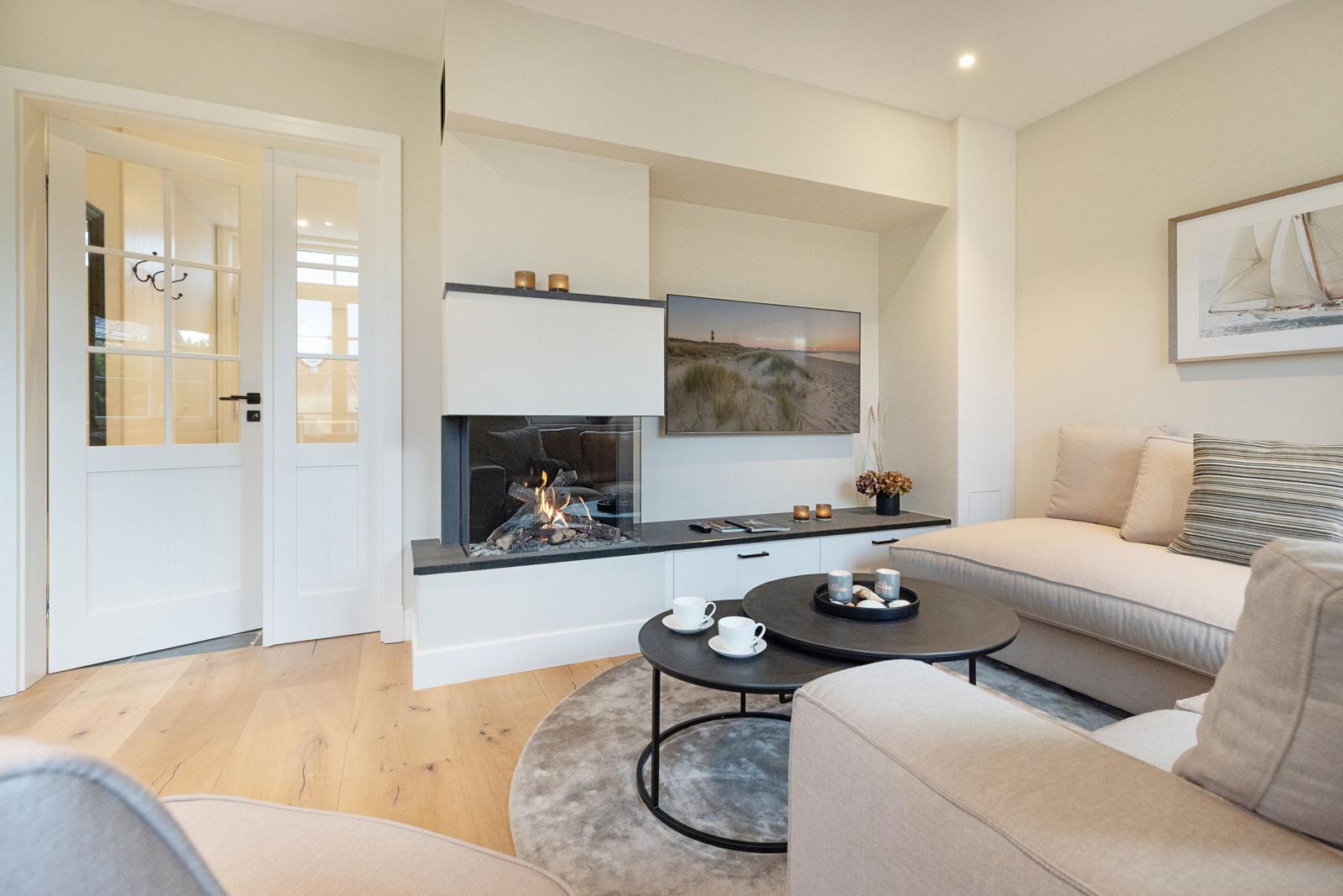 Wohnzimmer mit Kamin, Sofa und Fernseher. Holzboden und weiße Wände.