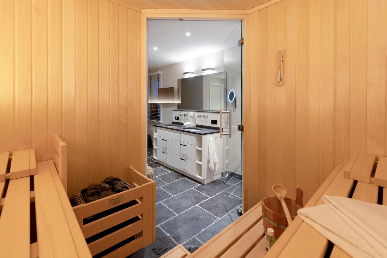 Sauna mit Holzbänken und Blick in das Badezimmer mit Waschbecken.