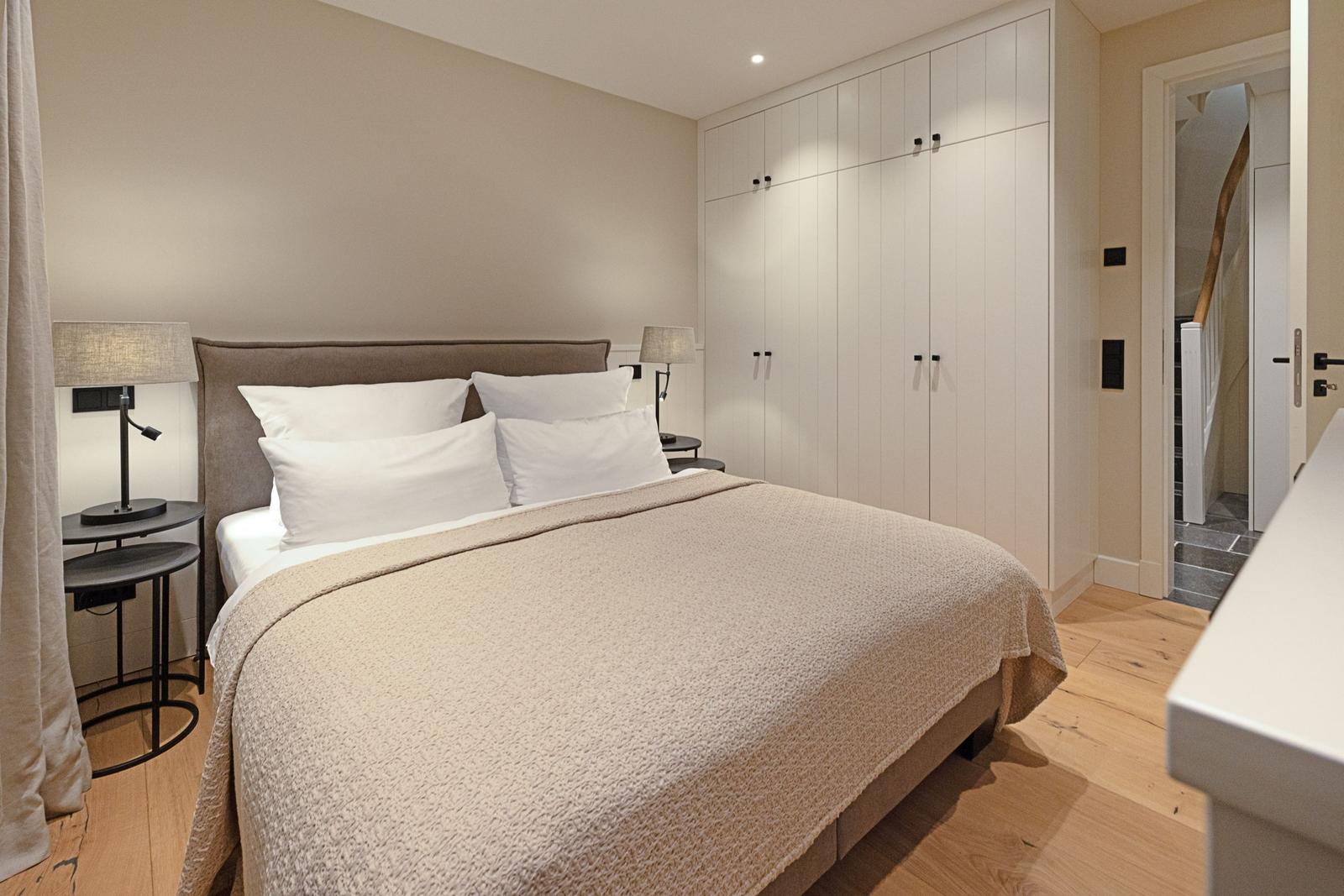 Schlafzimmer mit Bett, Nachttischen und Kleiderschrank. Holzboden und Tür zum Flur.