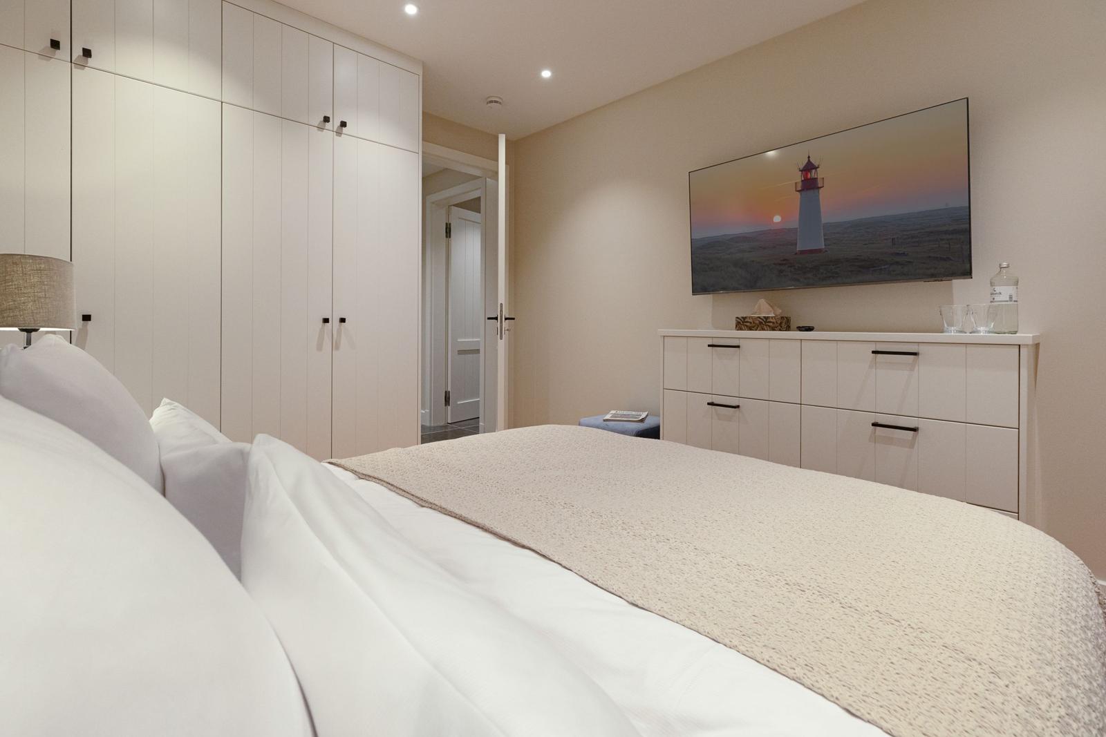 Schlafzimmer mit Bett, Kleiderschrank und Fernseher an der Wand.