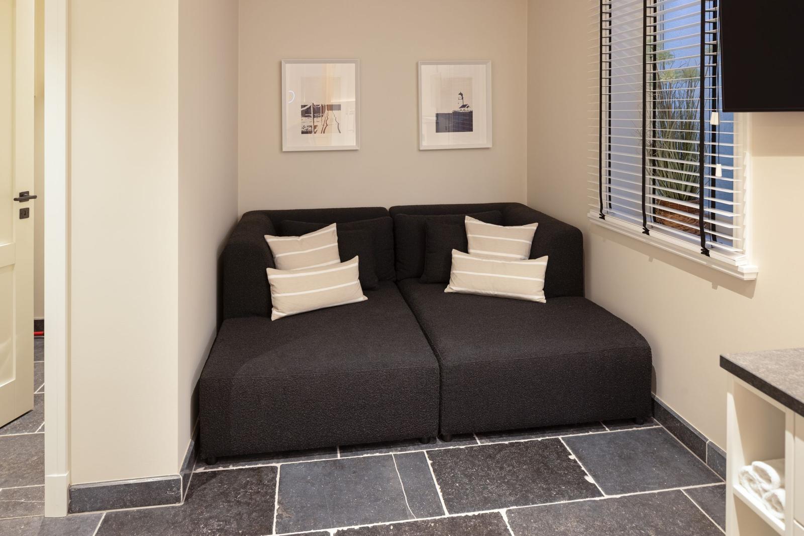 Schwarzes Sofa mit Kissen an Wand unter Fenster mit Jalousie.