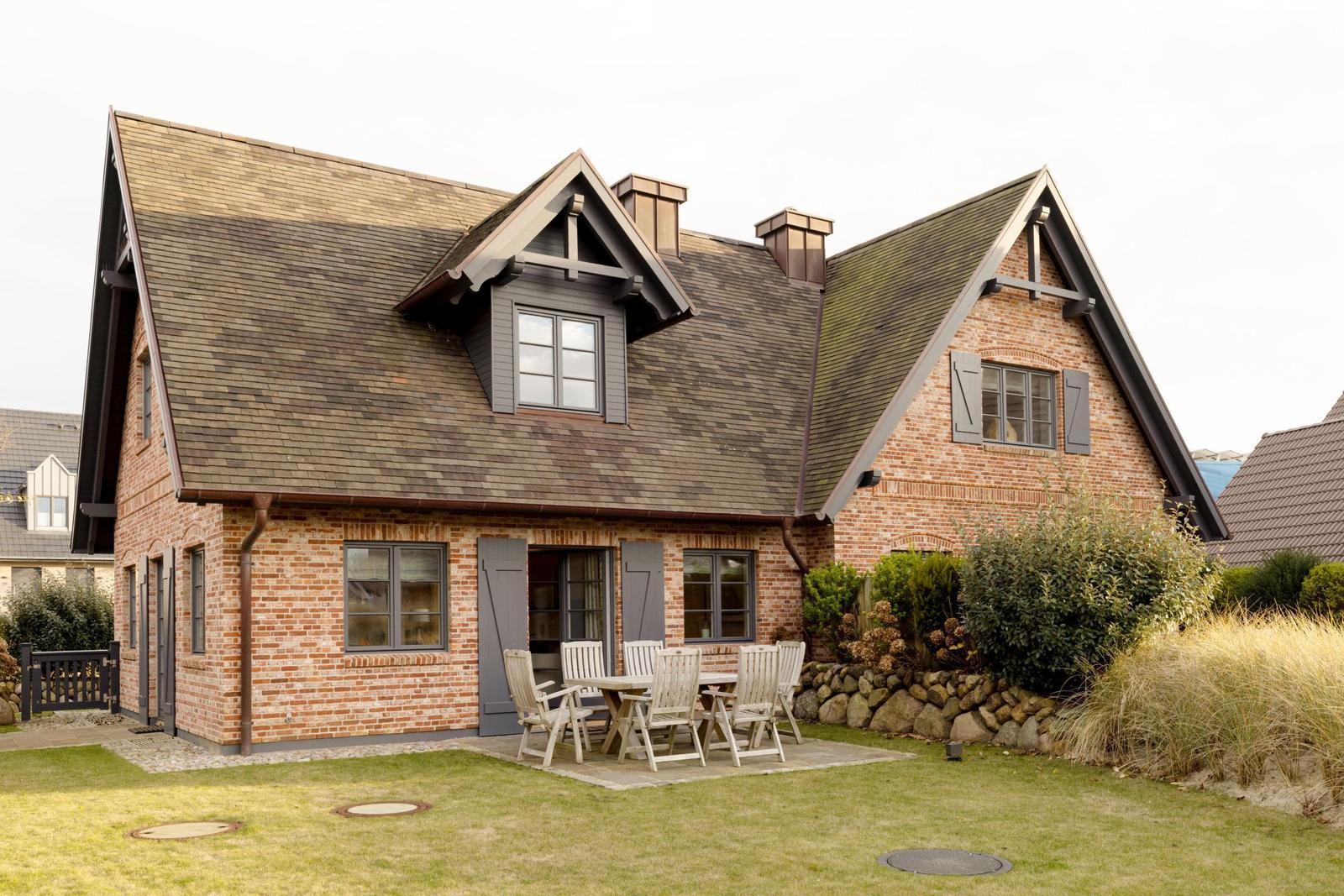 Ein Haus mit Backsteinfassade, dunklen Fenstern und einem Holzterrasse mit Tisch und Stühlen.