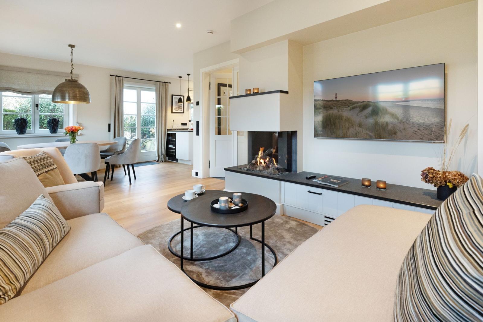 Wohnzimmer mit Kamin, Fernseher und Essbereich. Holzboden und moderne Einrichtung.
