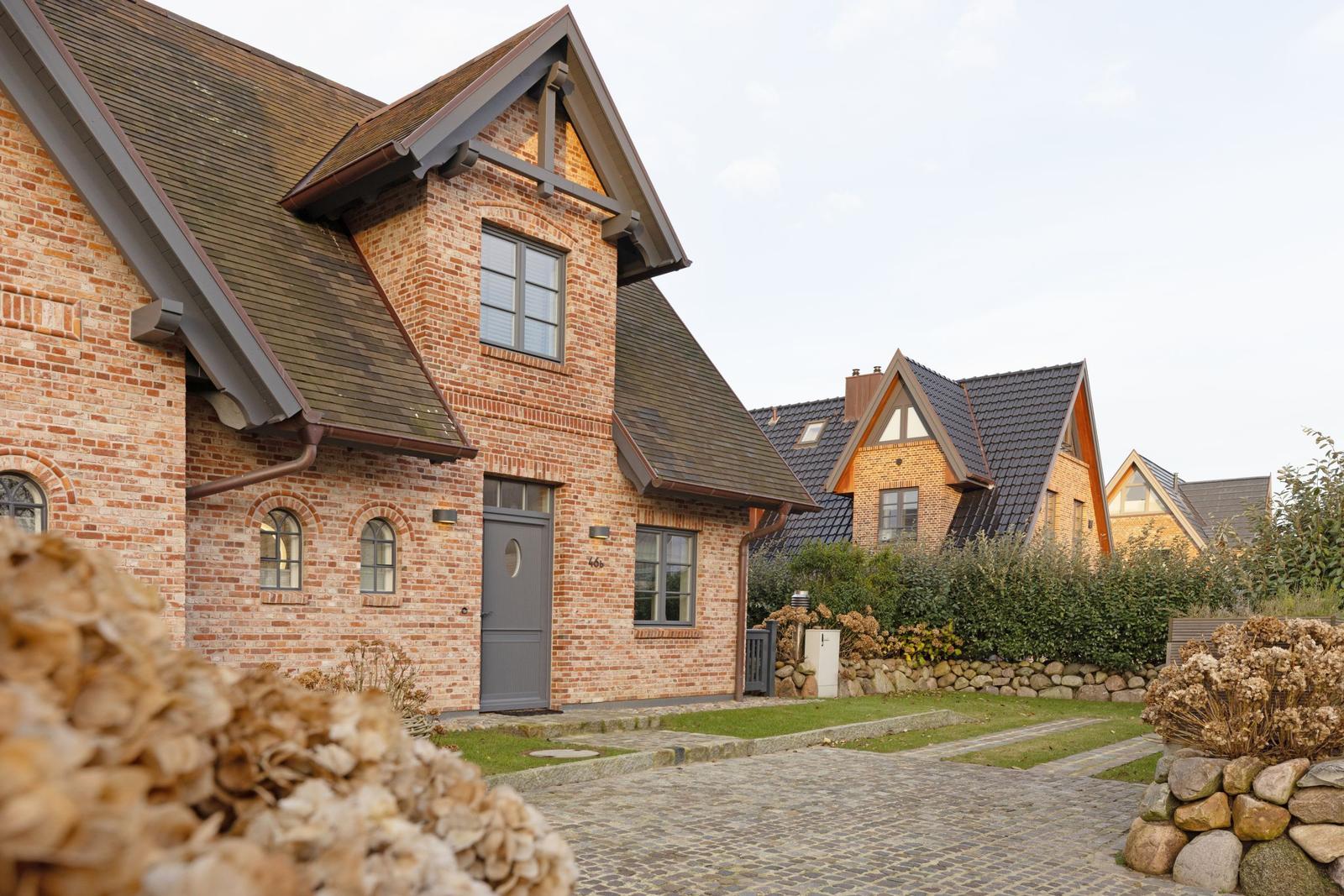 Haus mit Backsteinfassade und grauem Dach, gepflasterter Weg und Steinmauer