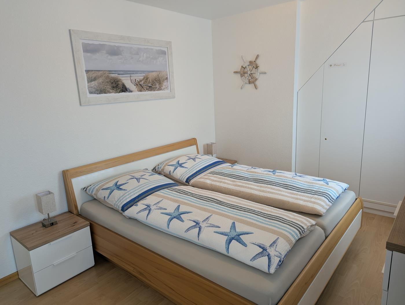 Schlafzimmer mit Bett, Nachttisch und Wandbild. Dekoration mit Segelruder und Strandmotiv.