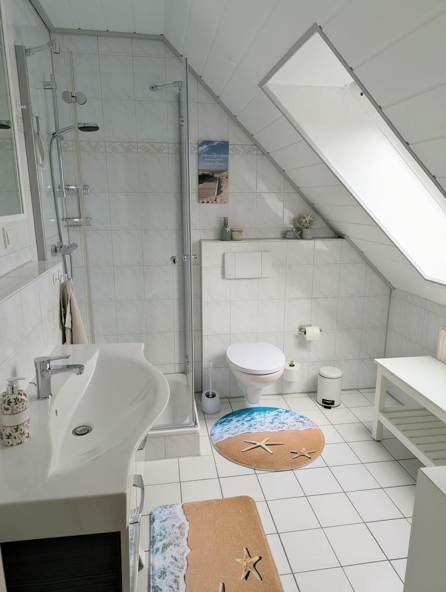 Badezimmer mit Dusche, Toilette und Waschbecken unter Dachschrägen.