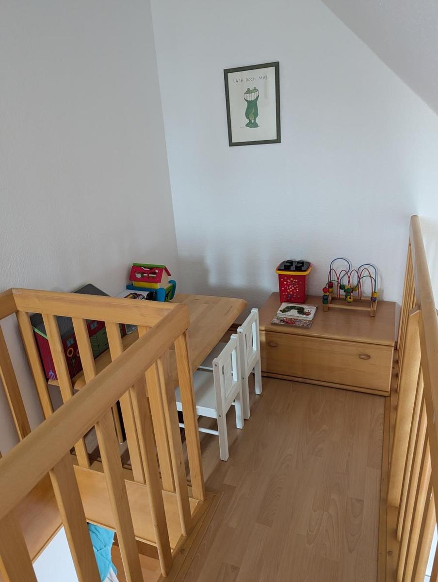 Kinderzimmer mit Holztisch, Stühlen und Spielzeug. An der Wand hängt ein Bild.