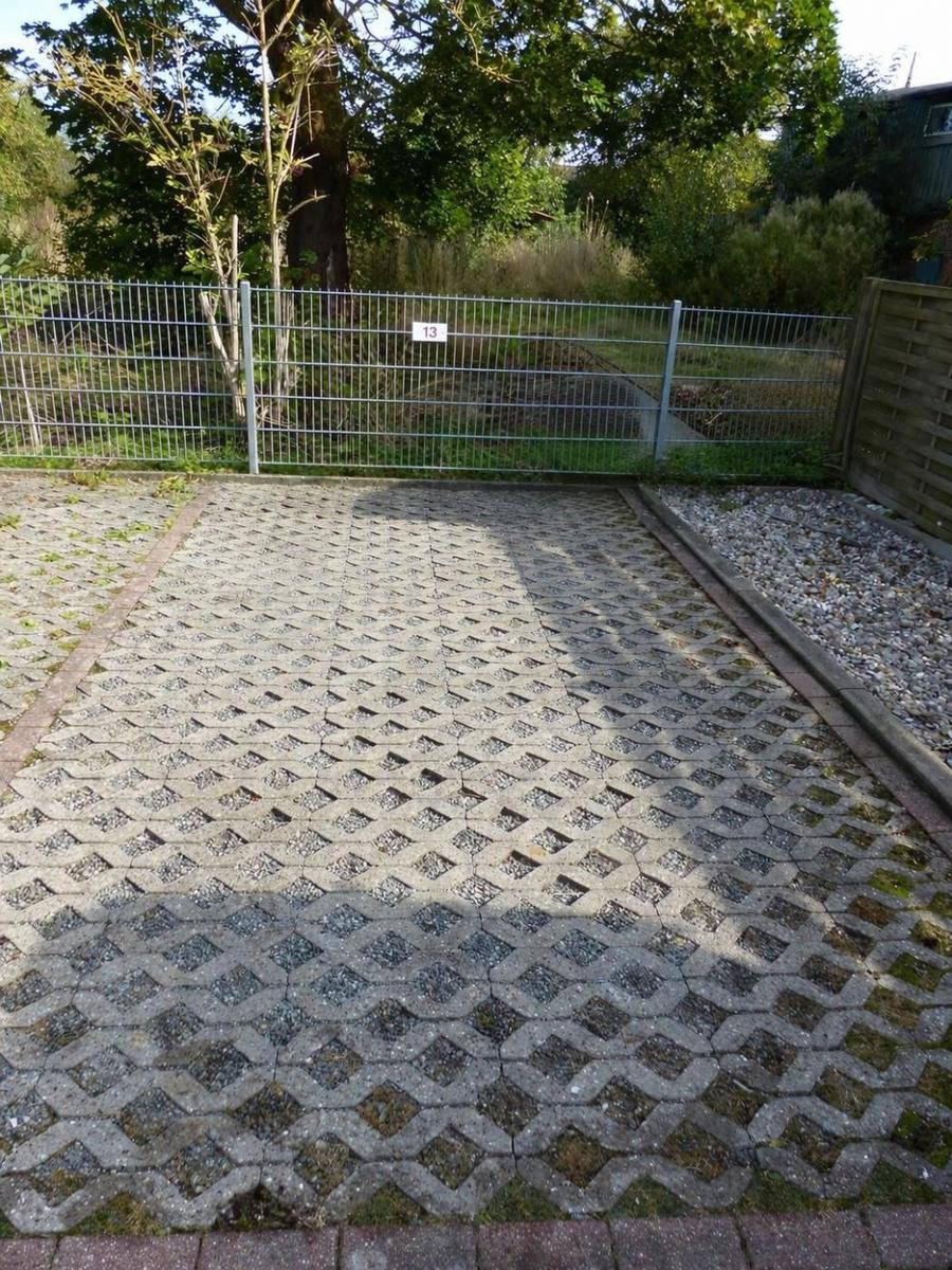 Pflasterter Weg führt zu einem Zaun mit Hausnummer 13. Gras und Bäume im Hintergrund.