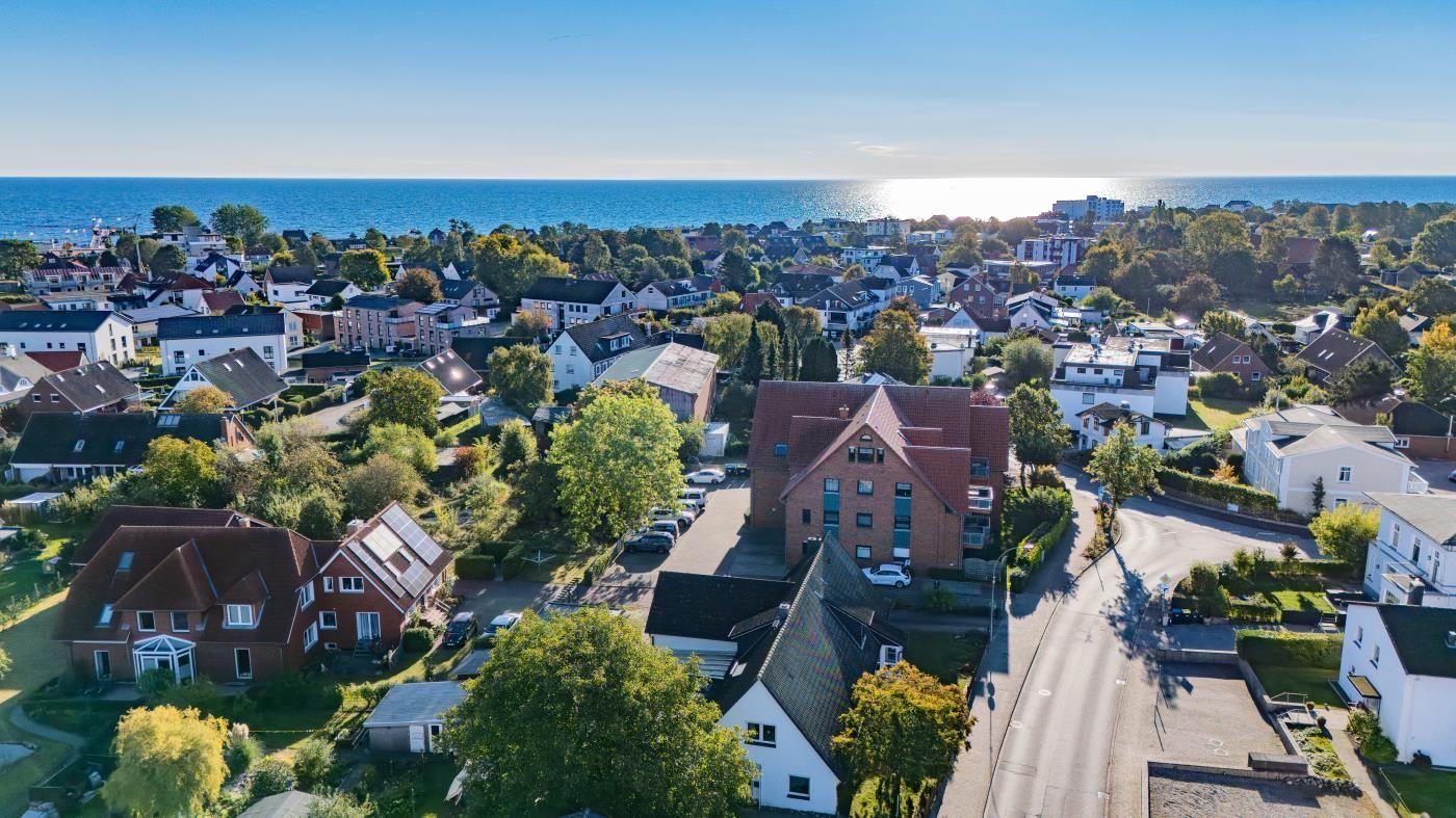 Aerial view of a coastal town with houses, trees, and the sea in the background.