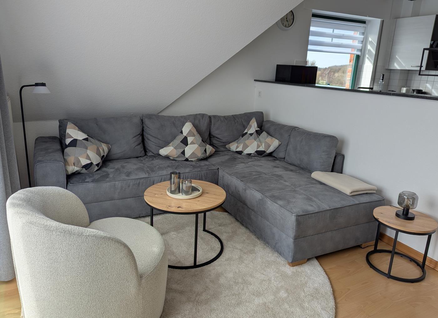Großer grauer Ecksofa mit Kissen, runder Tisch und Sessel im Wohnbereich.