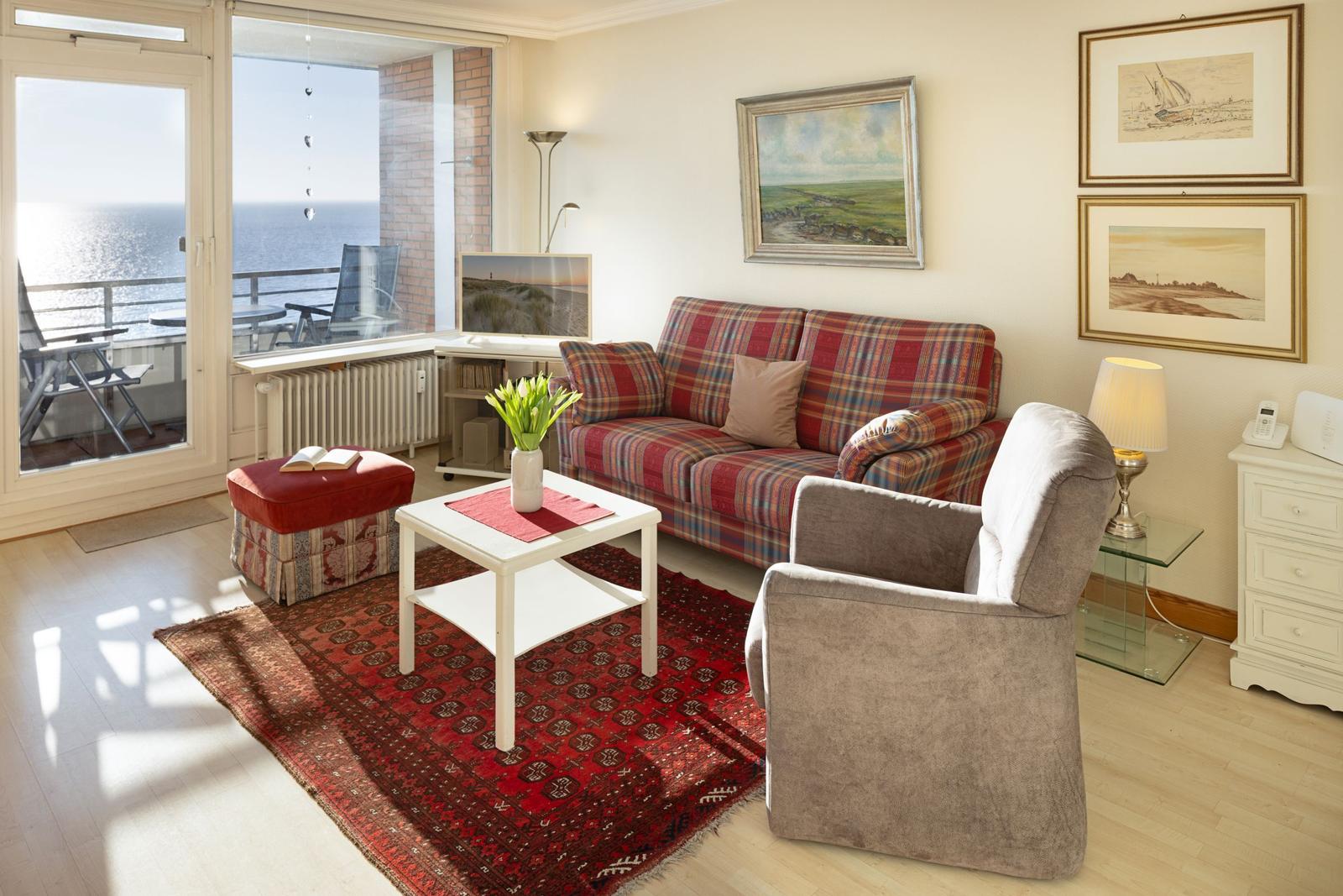 Wohnzimmer mit Sofa, Sessel und Balkonblick aufs Meer.