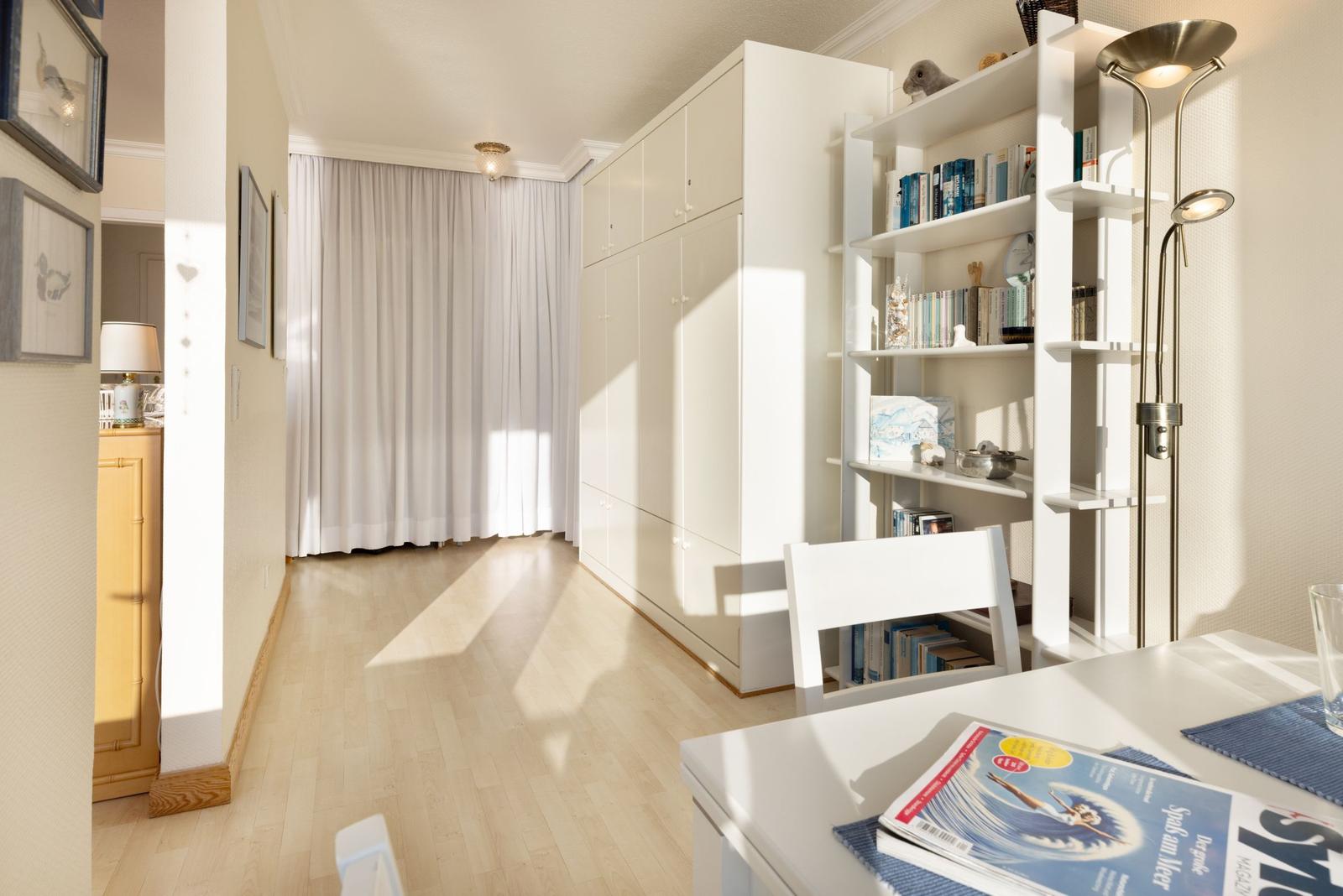 Wohnraum mit weißem Schrank, Bücherregal und Tisch mit Zeitschrift.