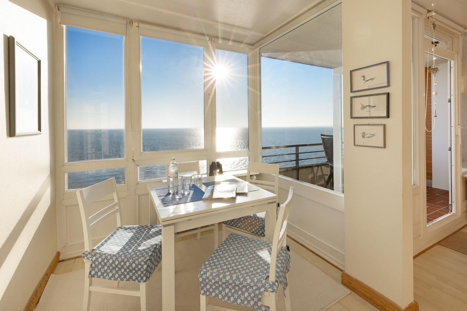 Essbereich mit Blick auf das Meer und Sonne. Tisch mit Stühlen und Fensterfront.