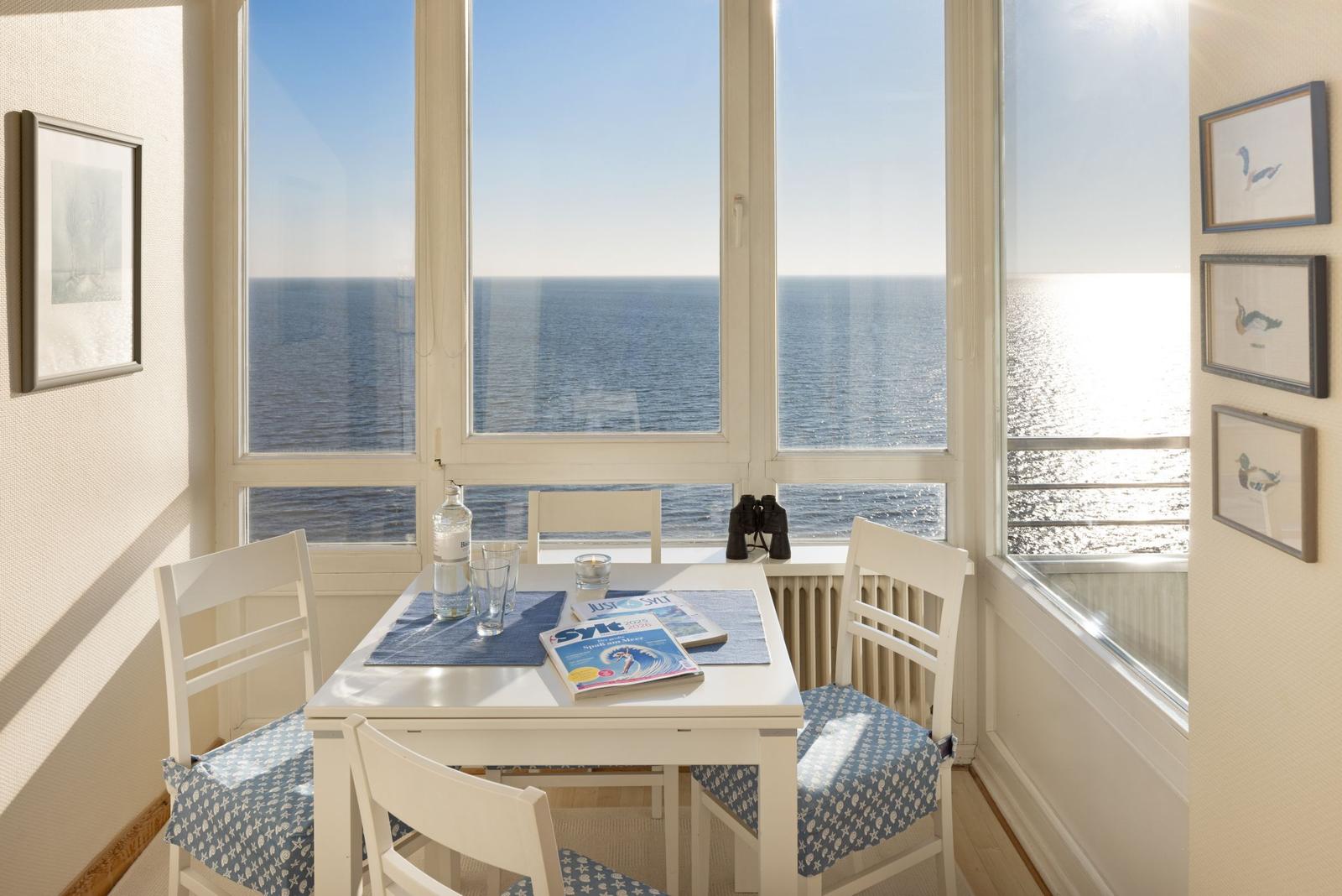 Esszimmer mit Blick auf das Meer, weißer Tisch und Stühle mit blauen Sitzkissen.