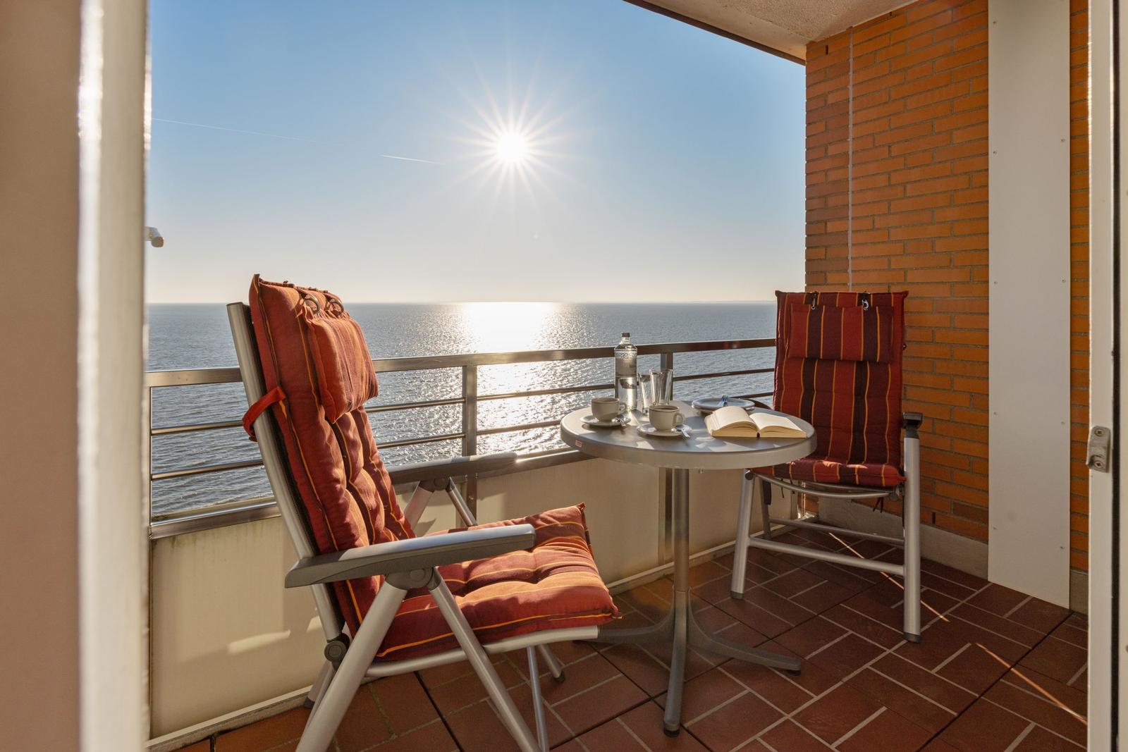 Terrasse mit Tisch und zwei Stühlen. Blick auf das Meer und die Sonne.