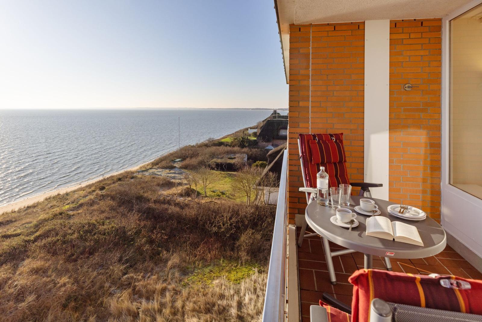 Terrasse mit Tisch und Stühlen, Blick auf Meer und Strand.
