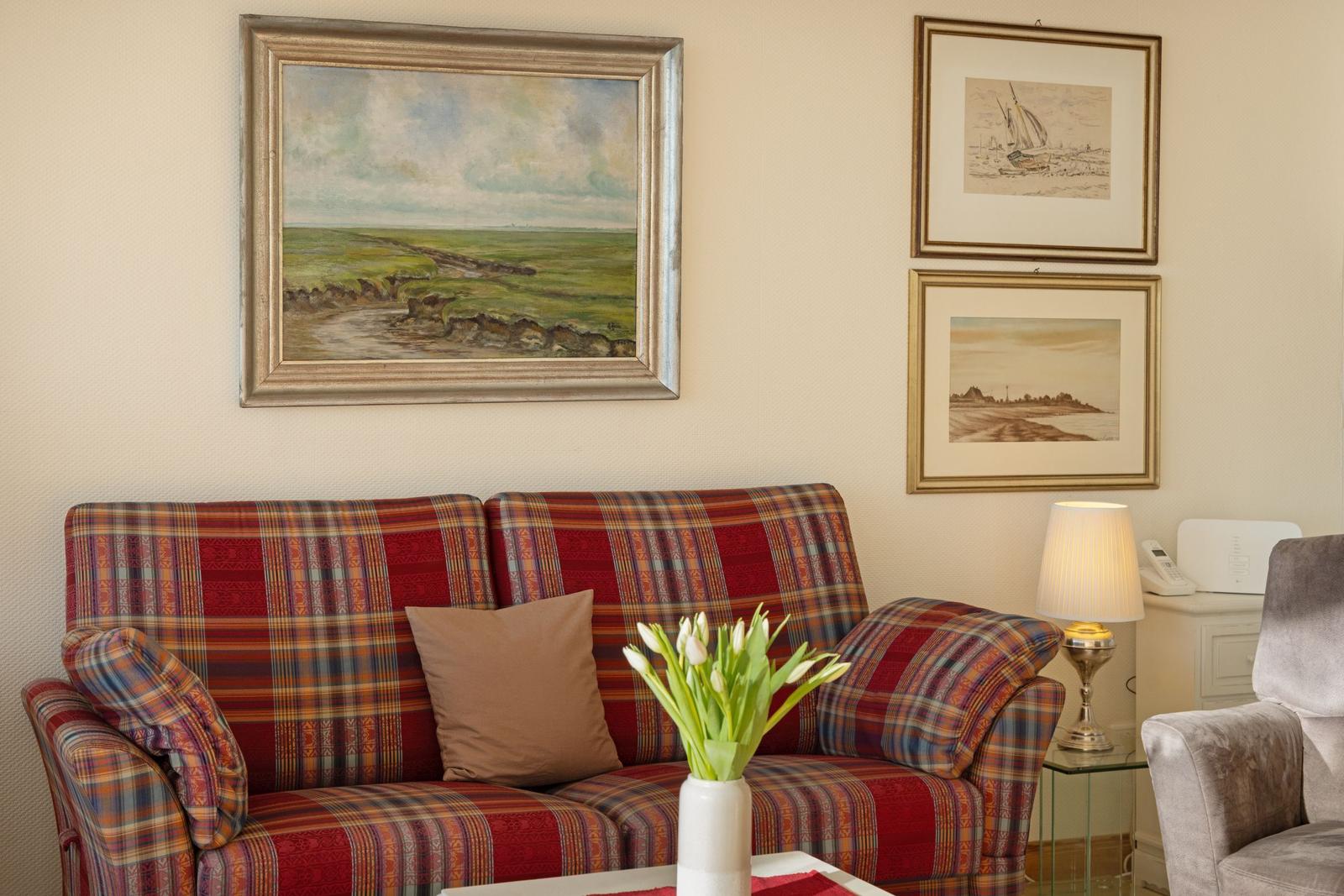 Ein Sofa mit kariertem Stoff, eine Vase mit Tulpen und Bilder an der Wand.