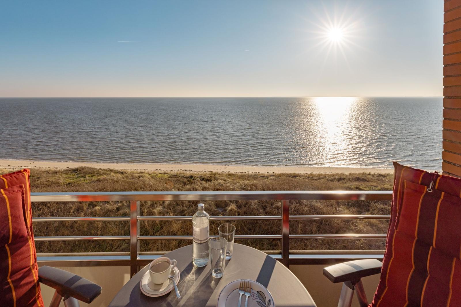 Balcony with table, chairs, and ocean view at sunrise.