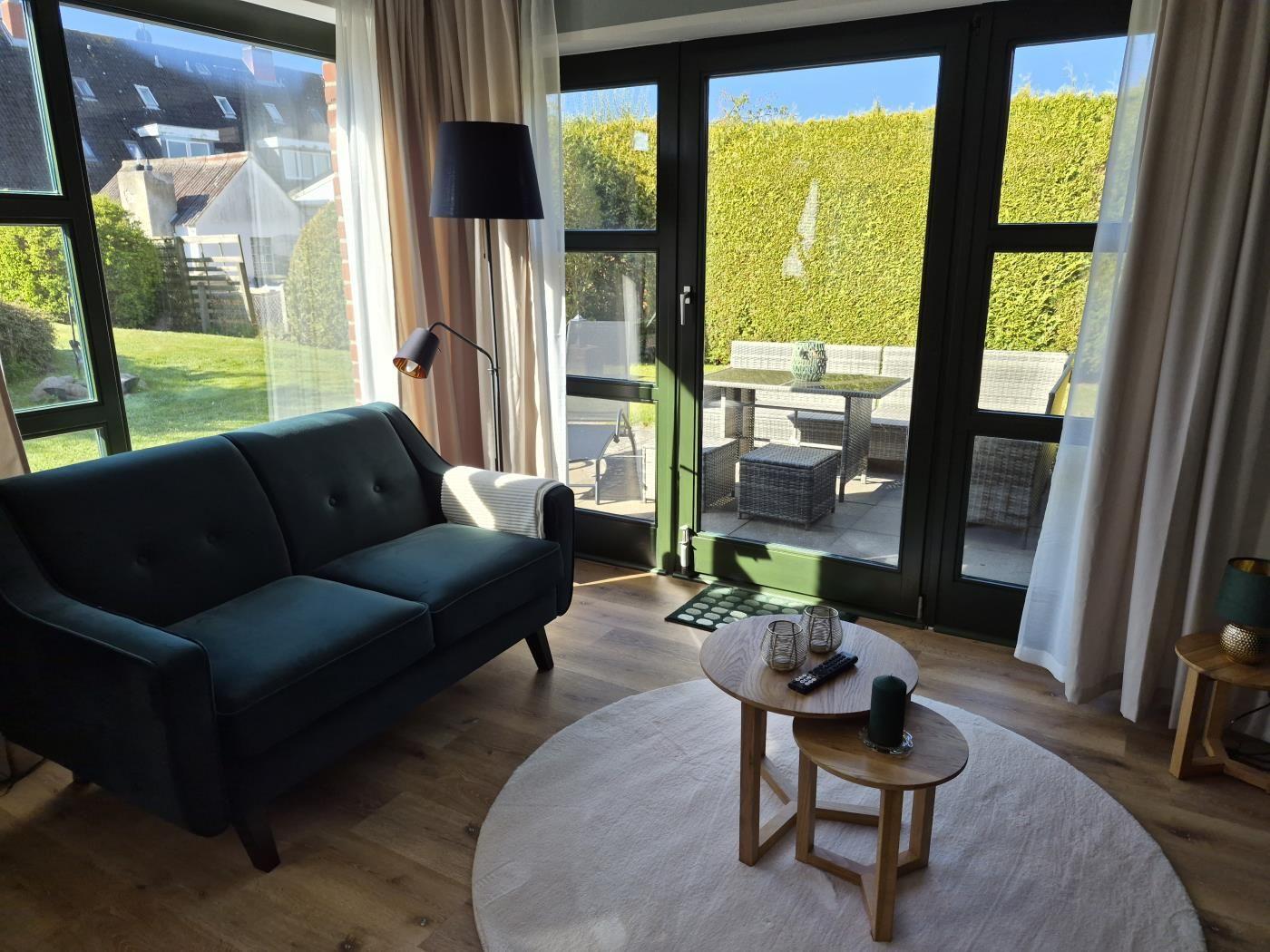 Ein Wohnzimmer mit dunklem Sofa, runden Tischen und großem Fenster zur Terrasse.