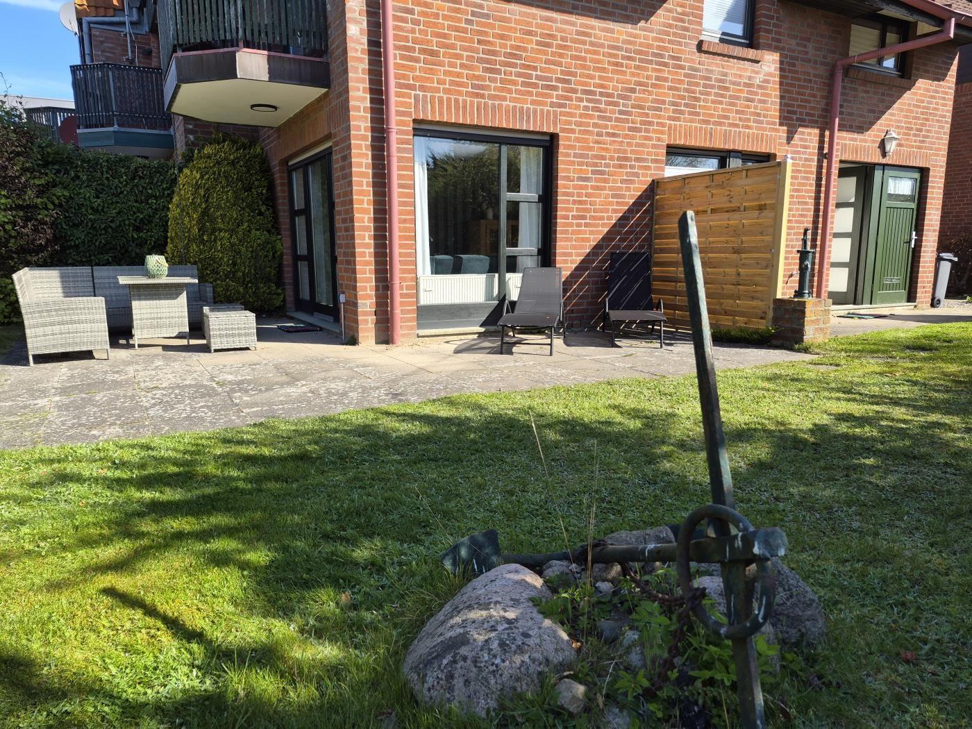Hinterhof mit Garten, Terrasse und Sitzgelegenheiten. Haus mit Backsteinfassade und Gartentür.