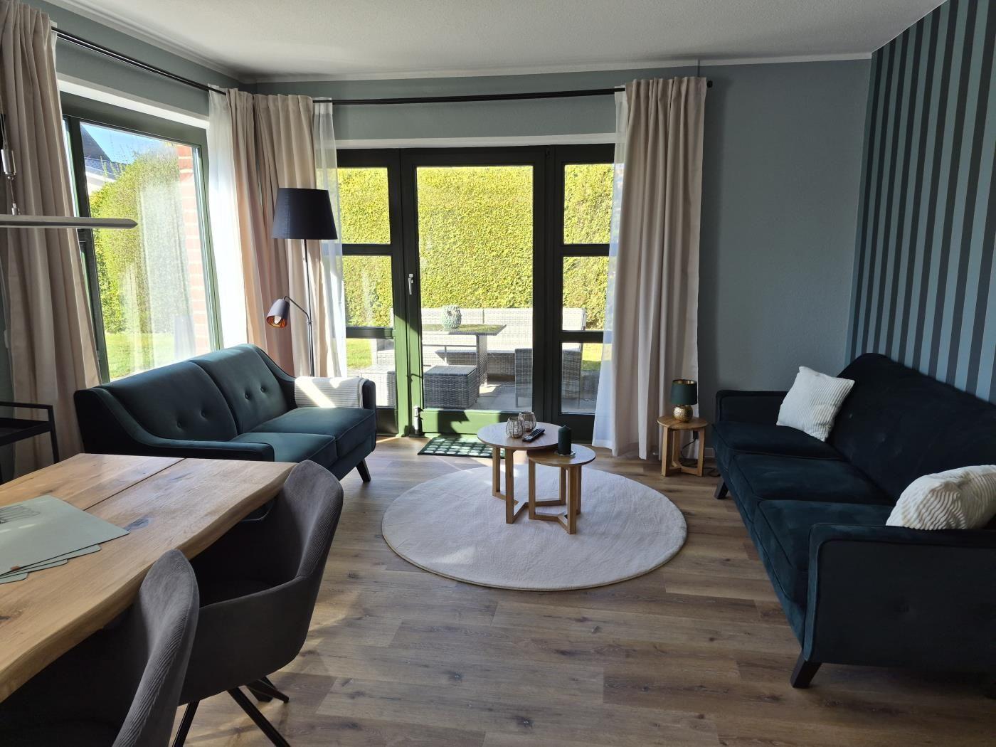 Wohnbereich mit zwei Sofas, runden Tisch und Blick auf den Garten.