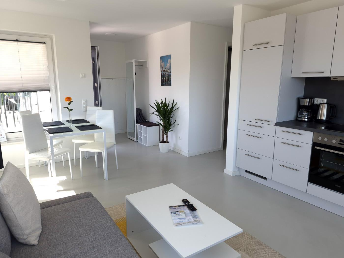 Wohnküche mit weißer Einbauküche, Esstisch und Sofa.