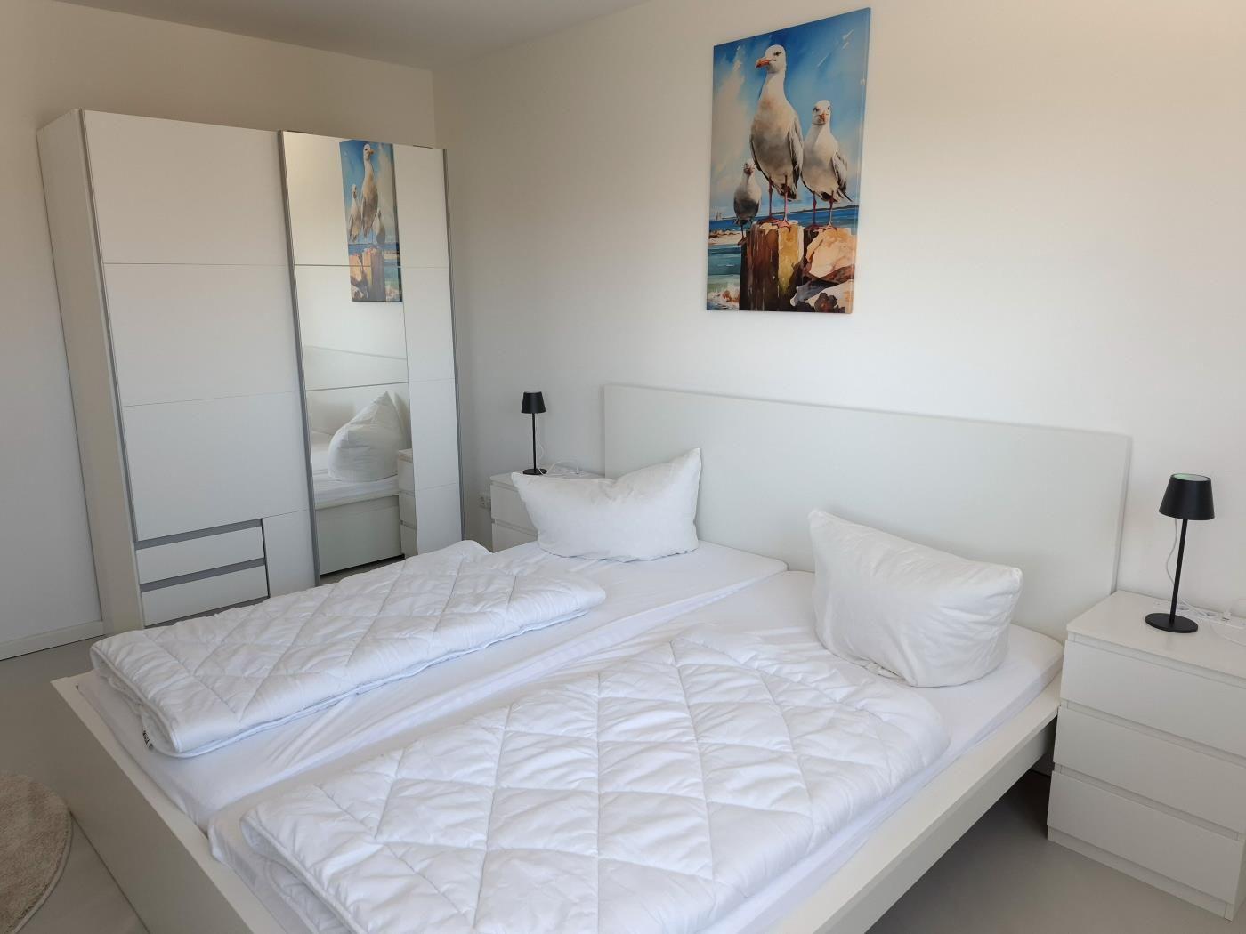 Schlafzimmer mit weißem Bett, Kleiderschrank und Wandbild mit Möwen.