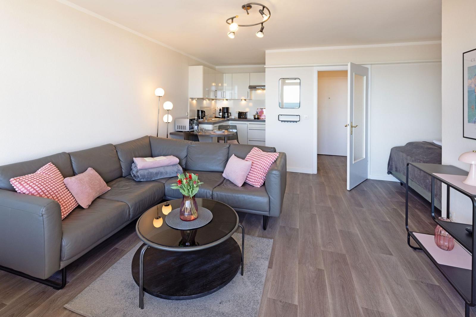 Wohnzimmer mit Sofa, Tisch und Küche im Hintergrund. Durchgang zur Schlafzimmer.