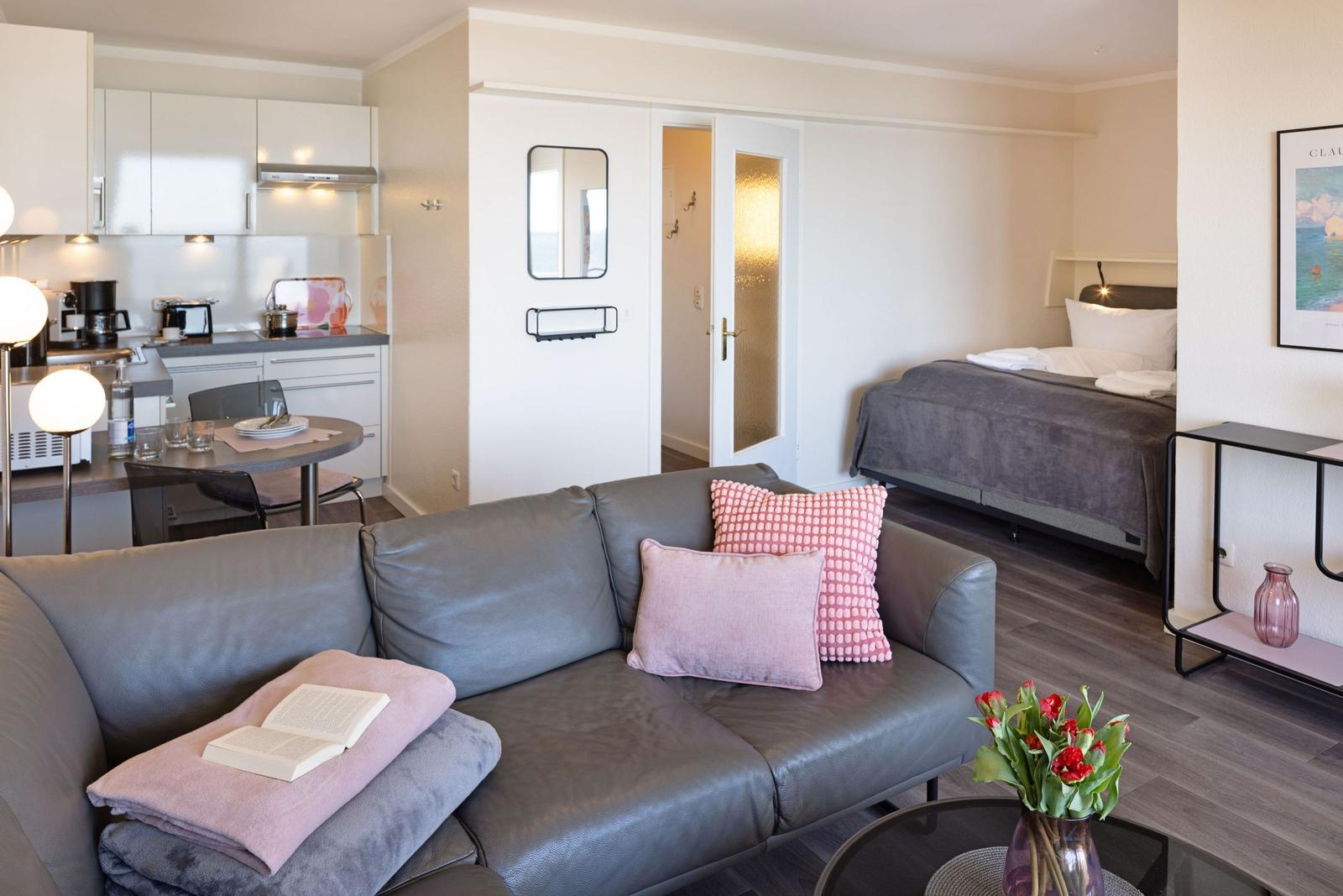 Wohnbereich mit Sofa, Küchenzeile und Schlafzimmer im Hintergrund.
